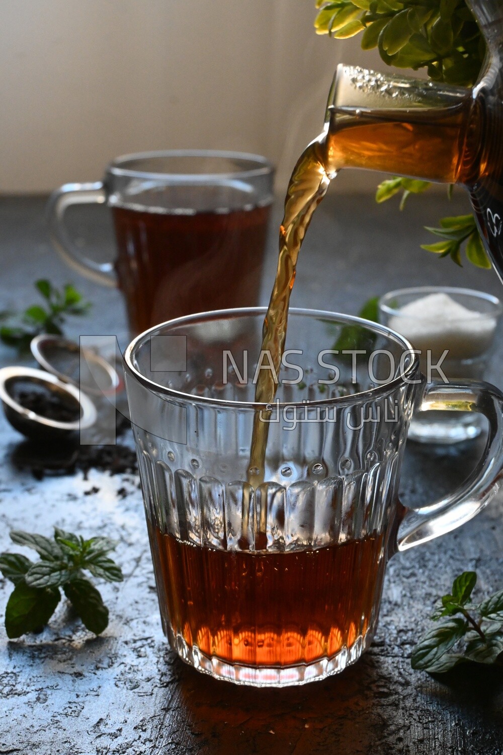 Glass kettle pouring tea from jug to cup of tea
