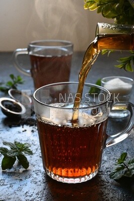 Glass kettle pouring tea from jug to cup of tea