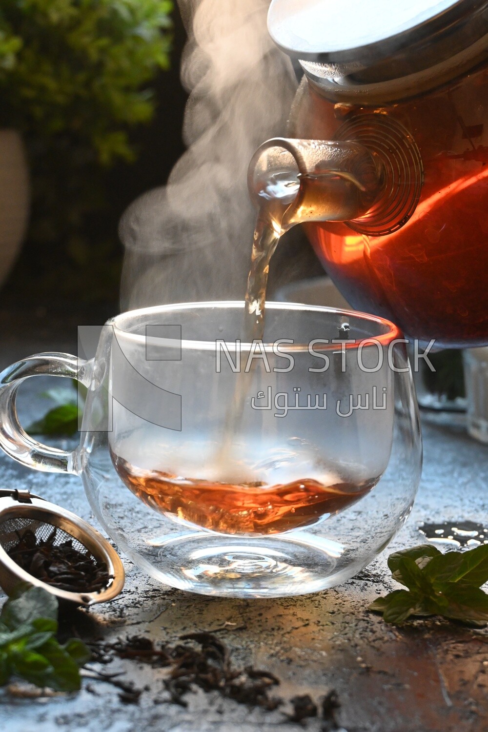 Glass kettle pouring tea from jug to cup of tea