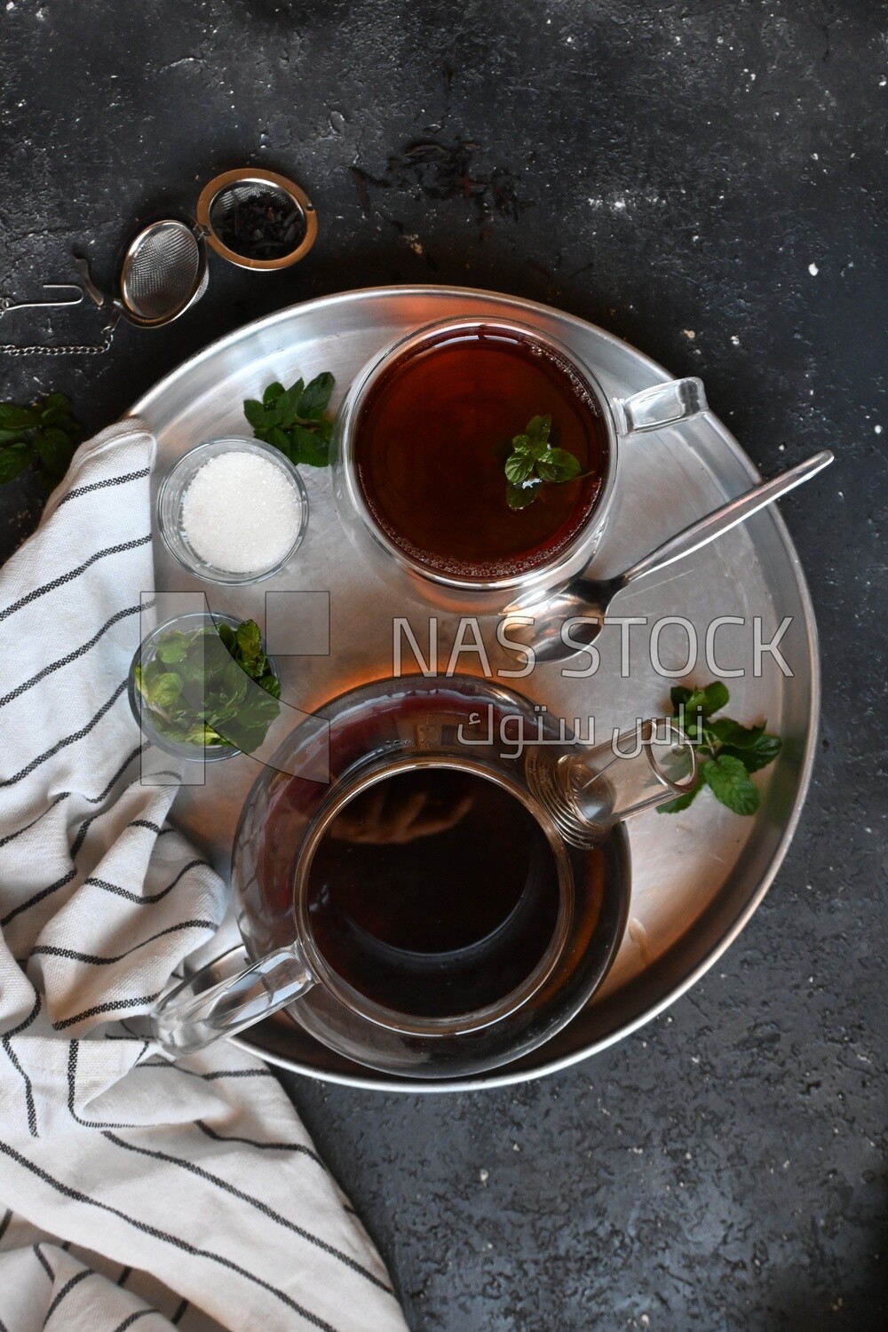 Cup of tea with a glass kettle, sugar, and a mint on a tray