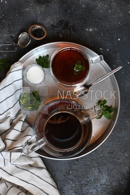 Cup of tea with a glass kettle, sugar, and a mint on a tray