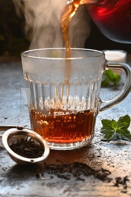 Glass kettle pouring tea from jug to cup of tea
