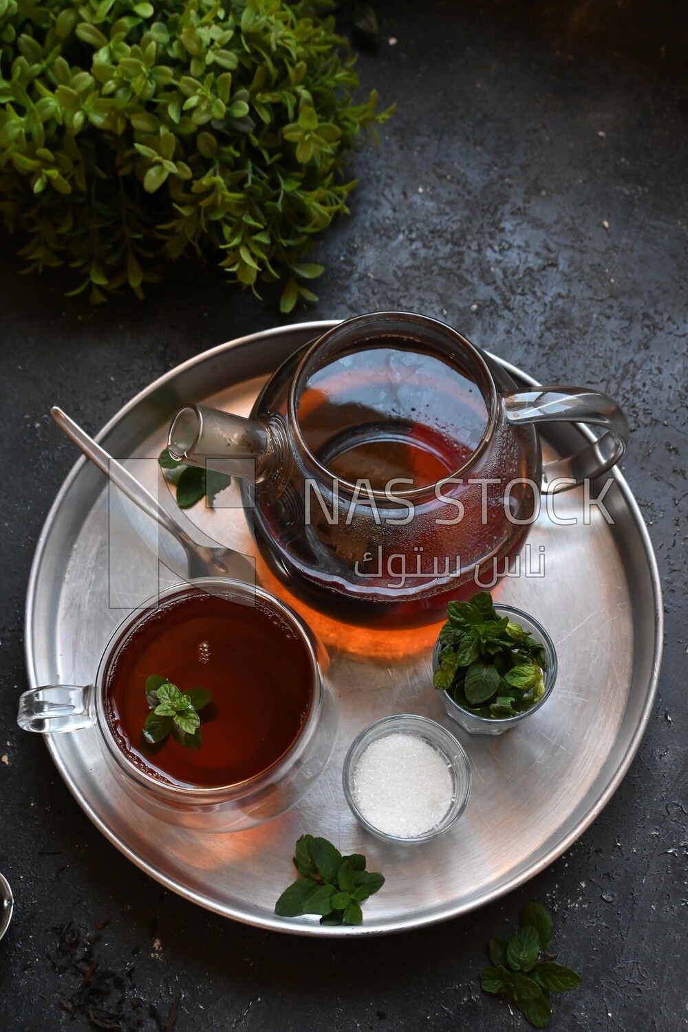 Cup of tea with a glass kettle, sugar, and a mint on a tray
