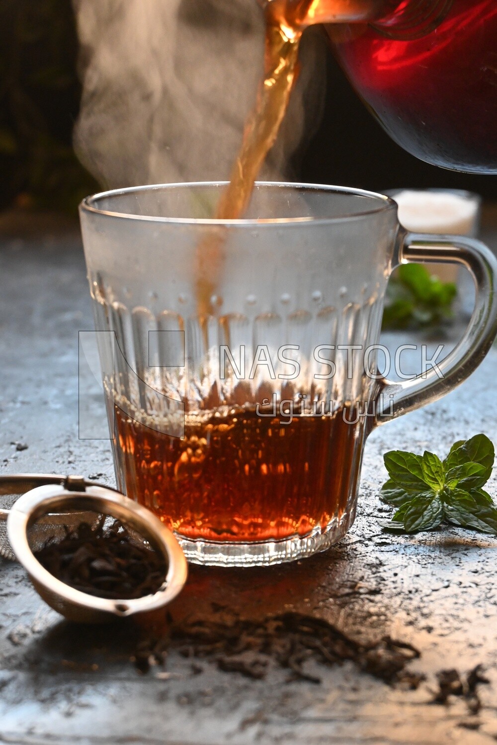 Glass kettle pouring tea from jug to cup of tea