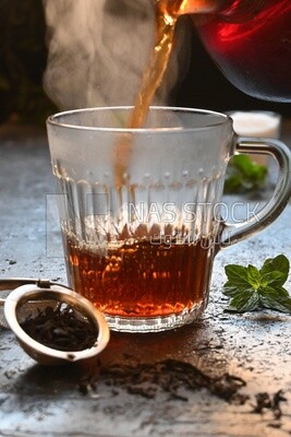 Glass kettle pouring tea from jug to cup of tea