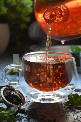 Glass kettle pouring tea from jug to cup of tea