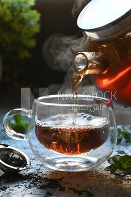Glass kettle pouring tea from jug to cup of tea