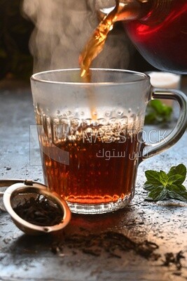 Glass kettle pouring tea from jug to cup of tea