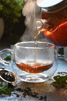 Glass kettle pouring tea from jug to cup of tea