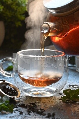 Glass kettle pouring tea from jug to cup of tea