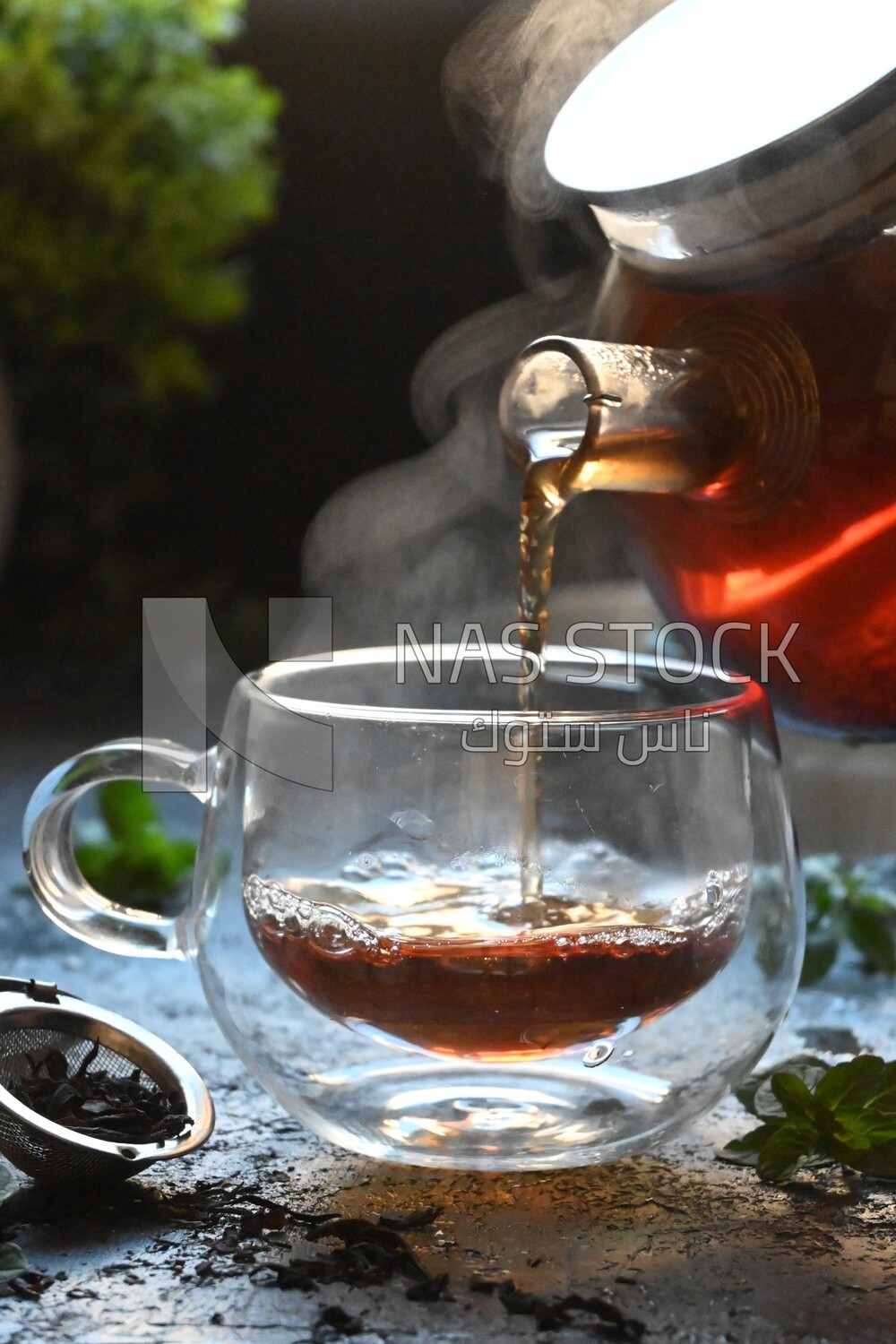 Glass kettle pouring tea from jug to cup of tea
