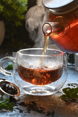 Glass kettle pouring tea from jug to cup of tea