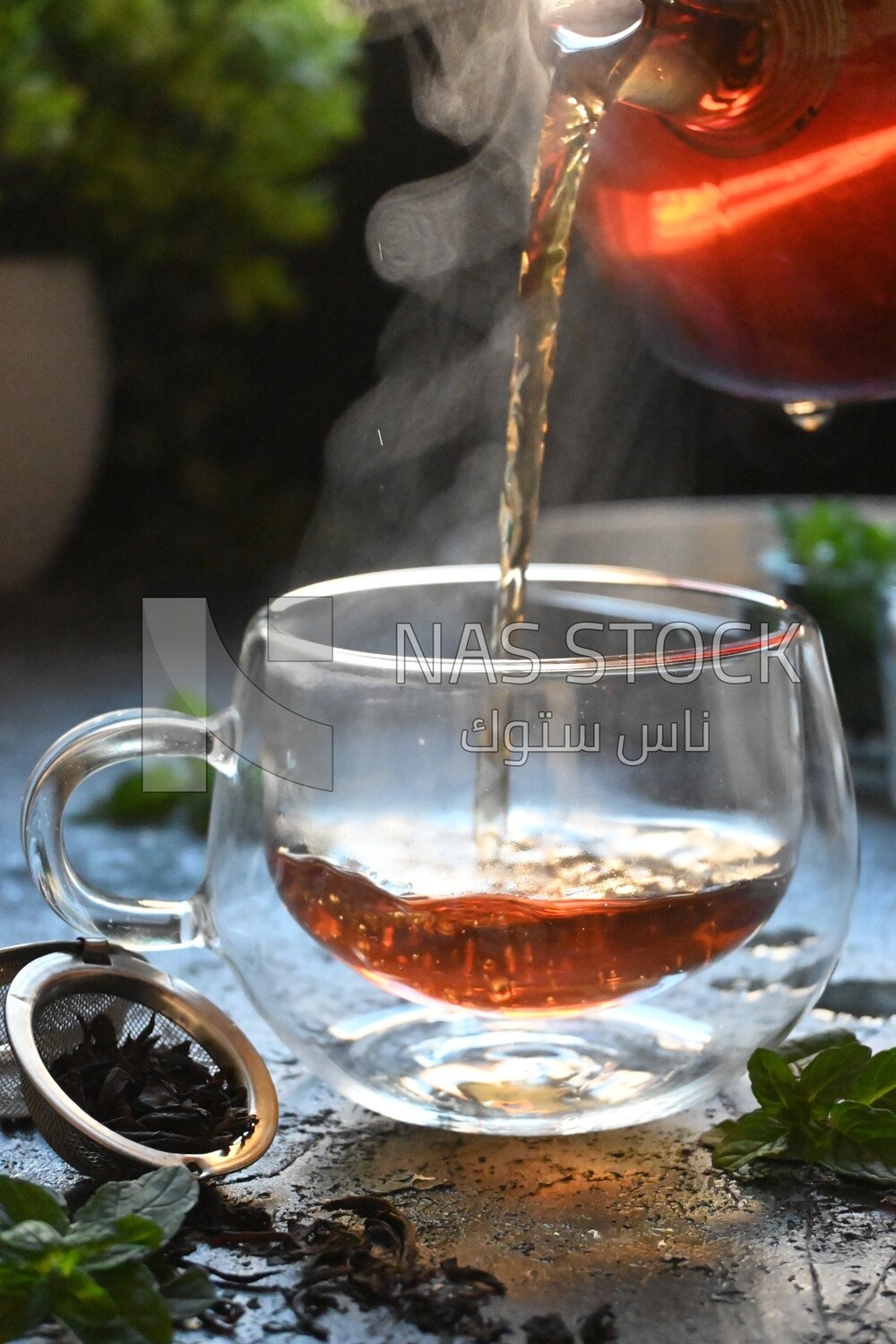 Glass kettle pouring tea from jug to cup of tea