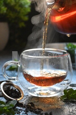 Glass kettle pouring tea from jug to cup of tea