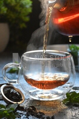 Glass kettle pouring tea from jug to cup of tea