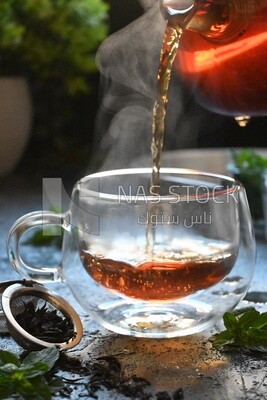 Glass kettle pouring tea from jug to cup of tea