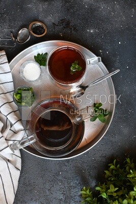 Cup of tea with a glass kettle, sugar, and a mint on a tray