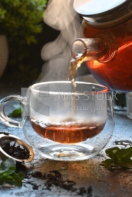 Glass kettle pouring tea from jug to cup of tea