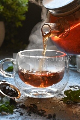 Glass kettle pouring tea from jug to cup of tea