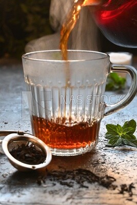 Glass kettle pouring tea from jug to cup of tea