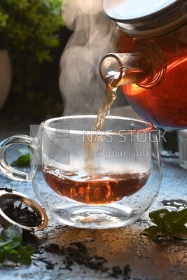 Glass kettle pouring tea from jug to cup of tea
