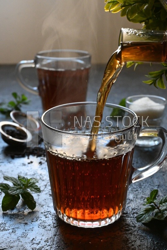 Glass kettle pouring tea from jug to cup of tea