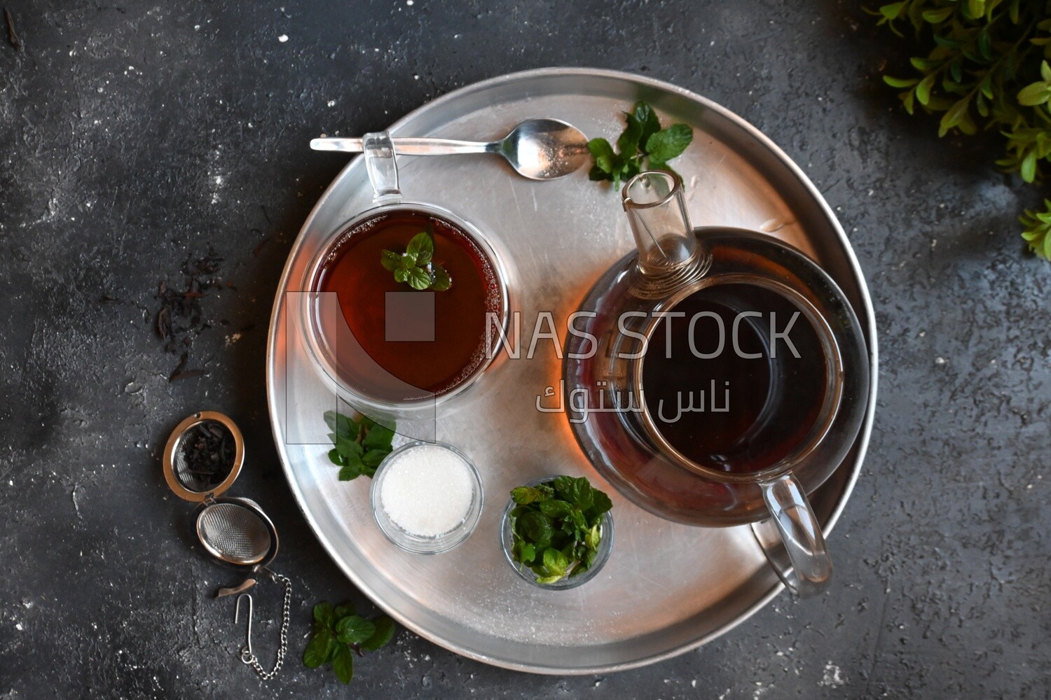 Cup of tea with a glass kettle, sugar, and a mint on a tray