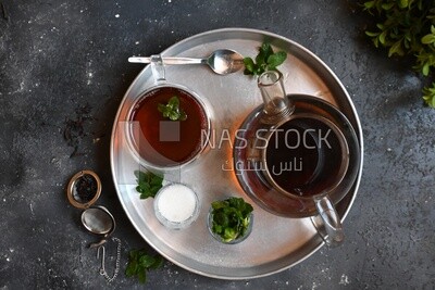 Cup of tea with a glass kettle, sugar, and a mint on a tray