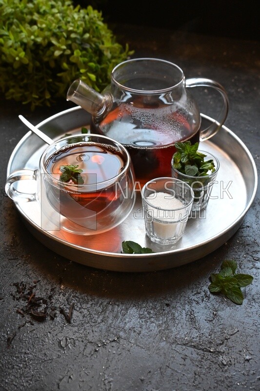Cup of tea with a glass kettle, sugar, and a mint on a tray