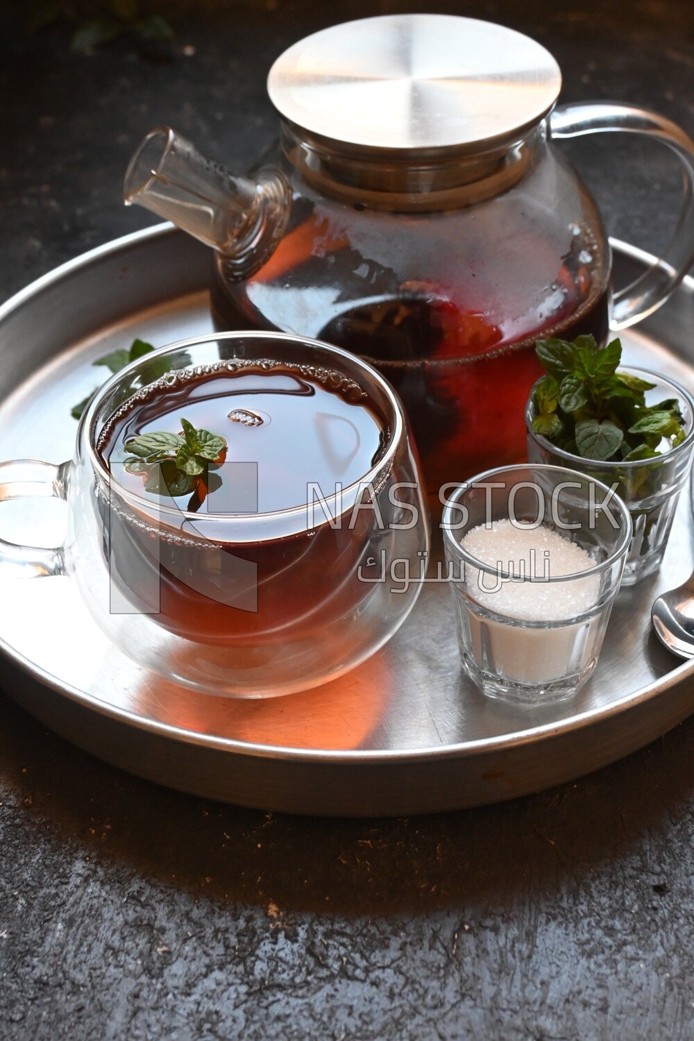 Cup of tea with a glass kettle, sugar, and a mint on a tray