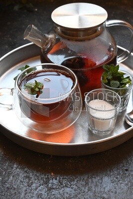 Cup of tea with a glass kettle, sugar, and a mint on a tray