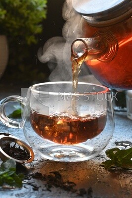 Glass kettle pouring tea from jug to cup of tea