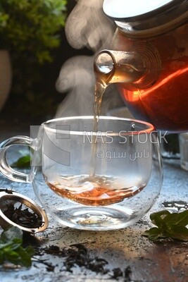 Glass kettle pouring tea from jug to cup of tea