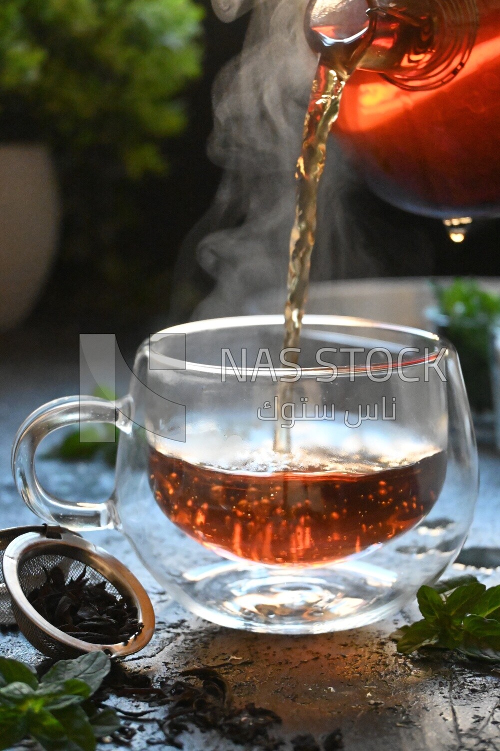 Glass kettle pouring tea from jug to cup of tea