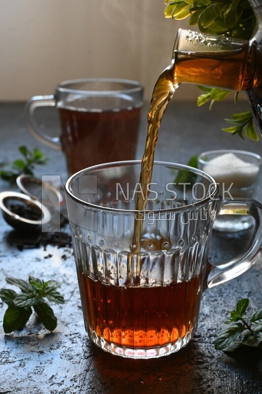 Glass kettle pouring tea from jug to cup of tea