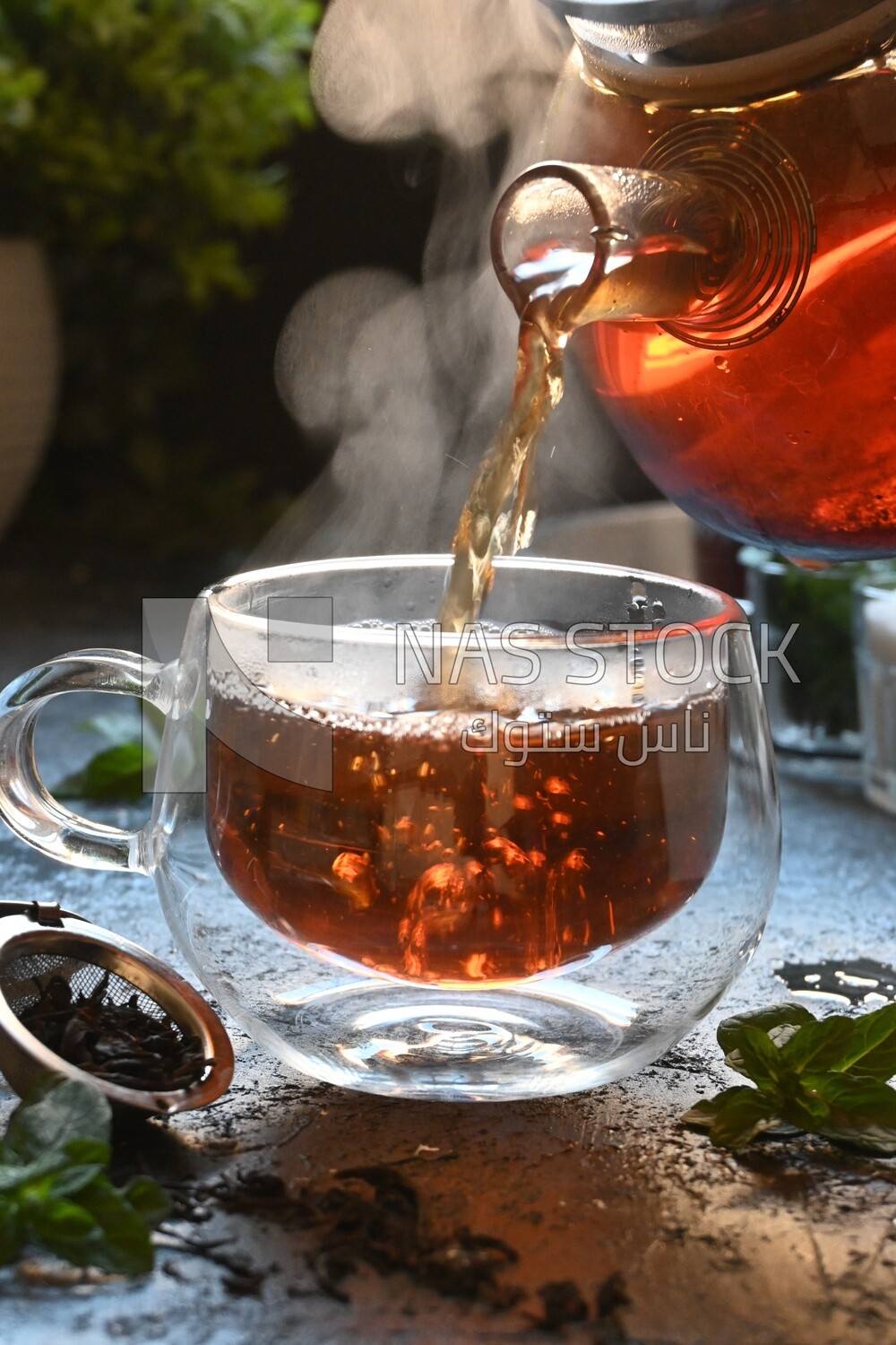 Glass kettle pouring tea from jug to cup of tea