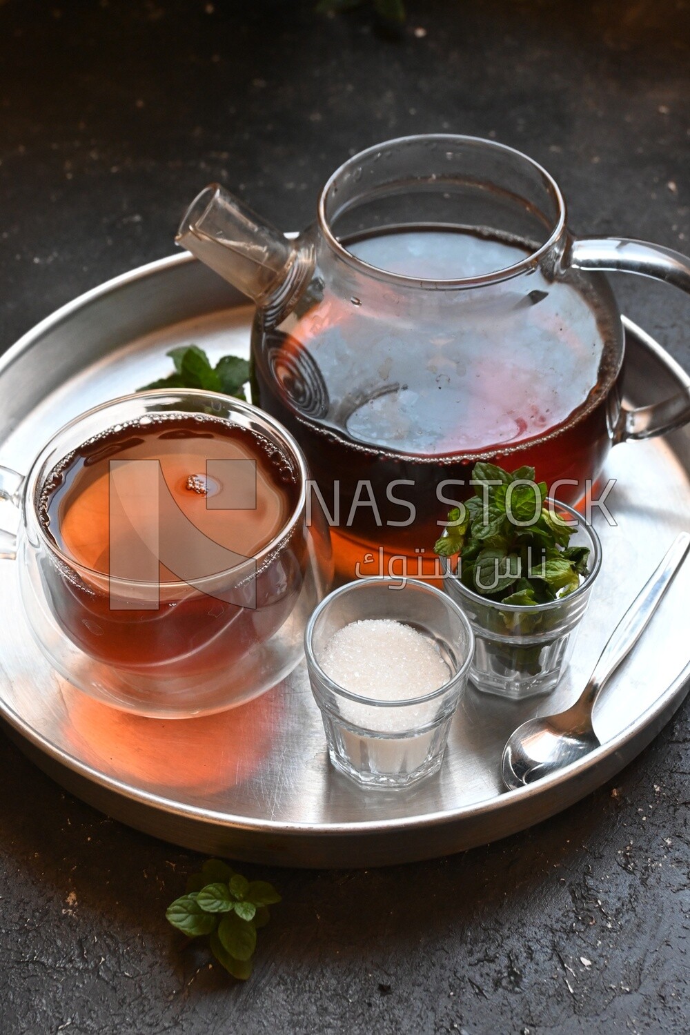 Cup of tea with a glass kettle, sugar, and a mint on a tray