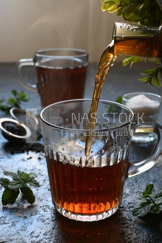 Glass kettle pouring tea from jug to cup of tea