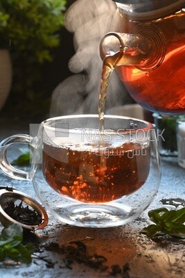 Glass kettle pouring tea from jug to cup of tea