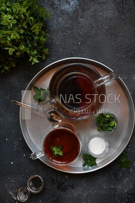Cup of tea with a glass kettle, sugar, and a mint on a tray