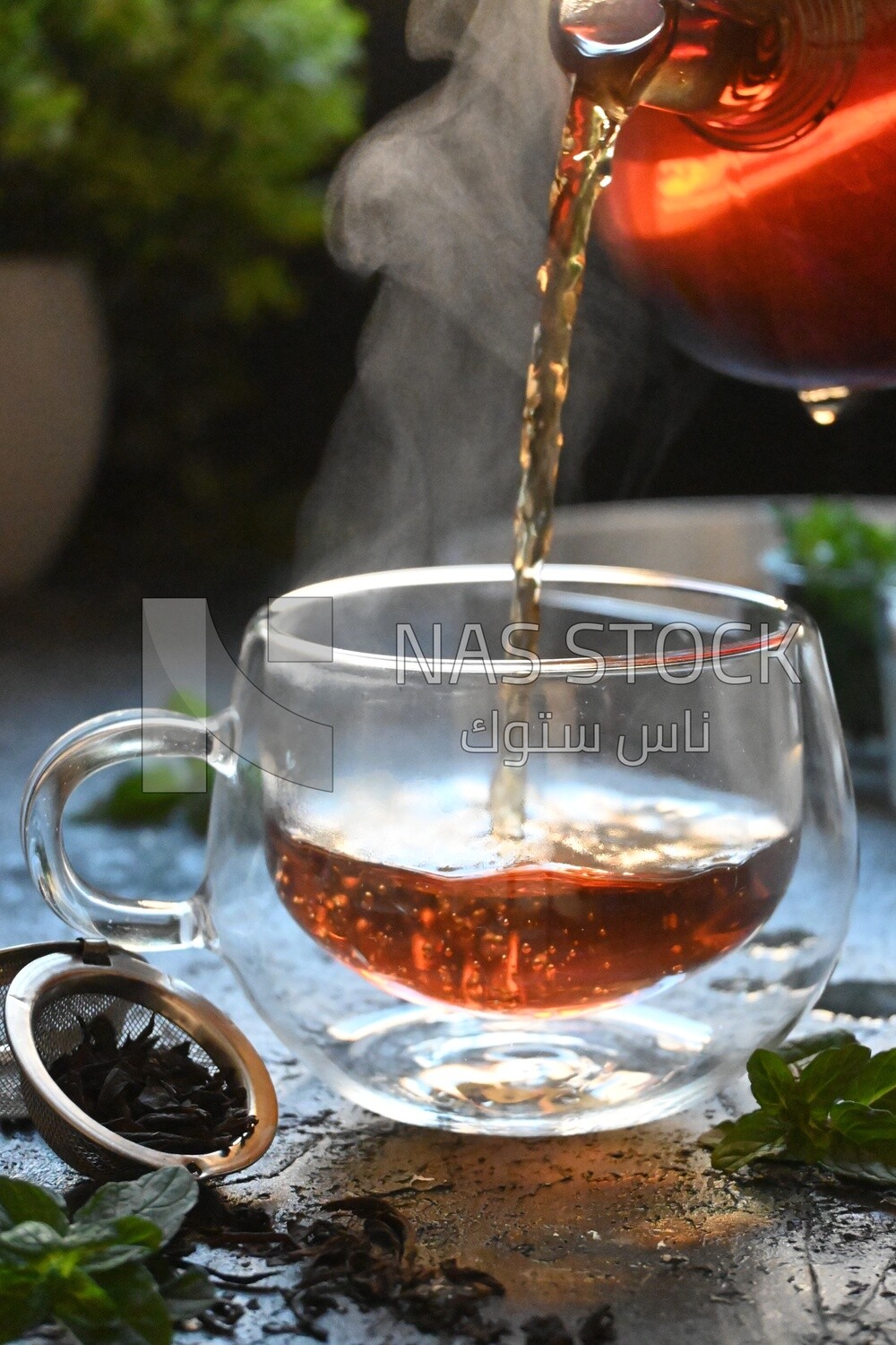 Glass kettle pouring tea from jug to cup of tea