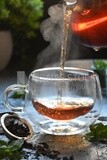 Glass kettle pouring tea from jug to cup of tea