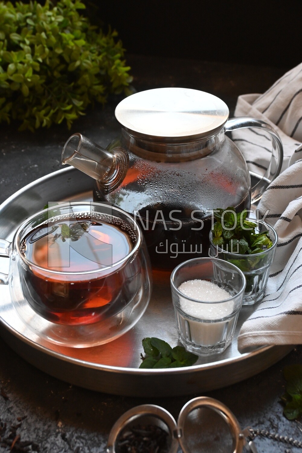 Cup of tea with a glass kettle, sugar, and a mint on a tray