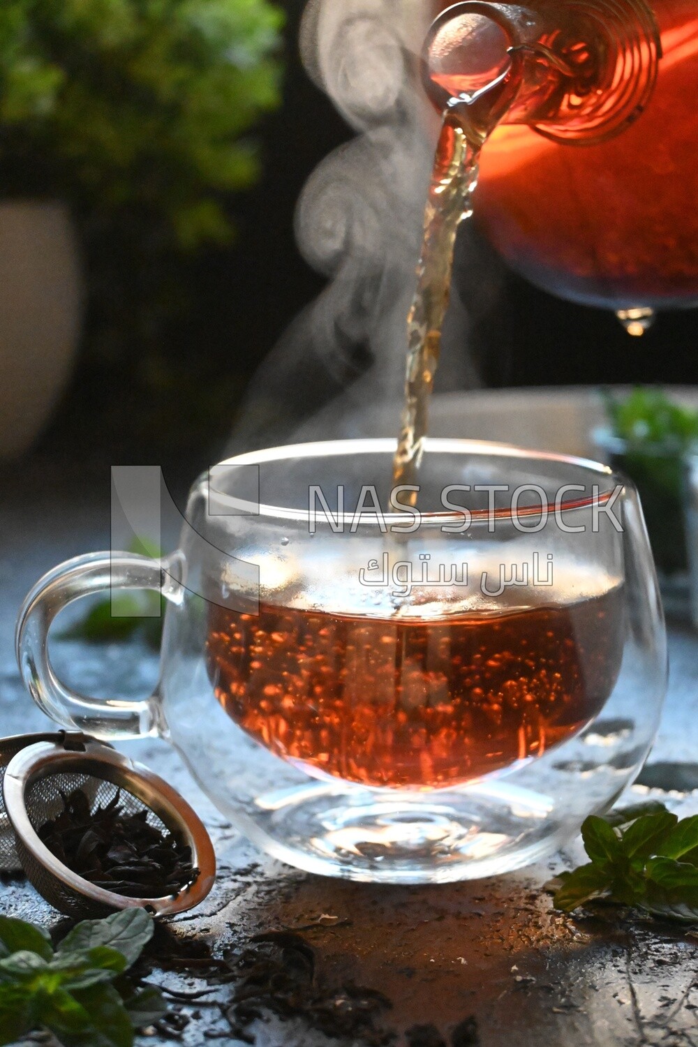 Glass kettle pouring tea from jug to cup of tea