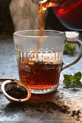 Glass kettle pouring tea from jug to cup of tea