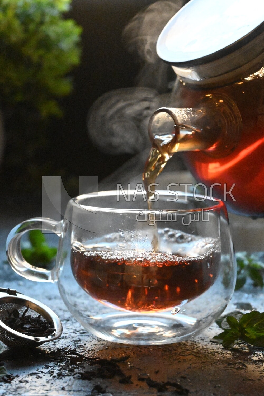 Glass kettle pouring tea from jug to cup of tea