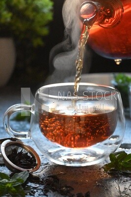 Glass kettle pouring tea from jug to cup of tea