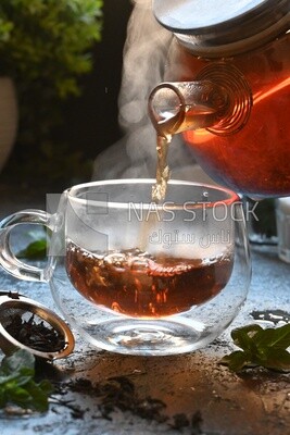 Glass kettle pouring tea from jug to cup of tea