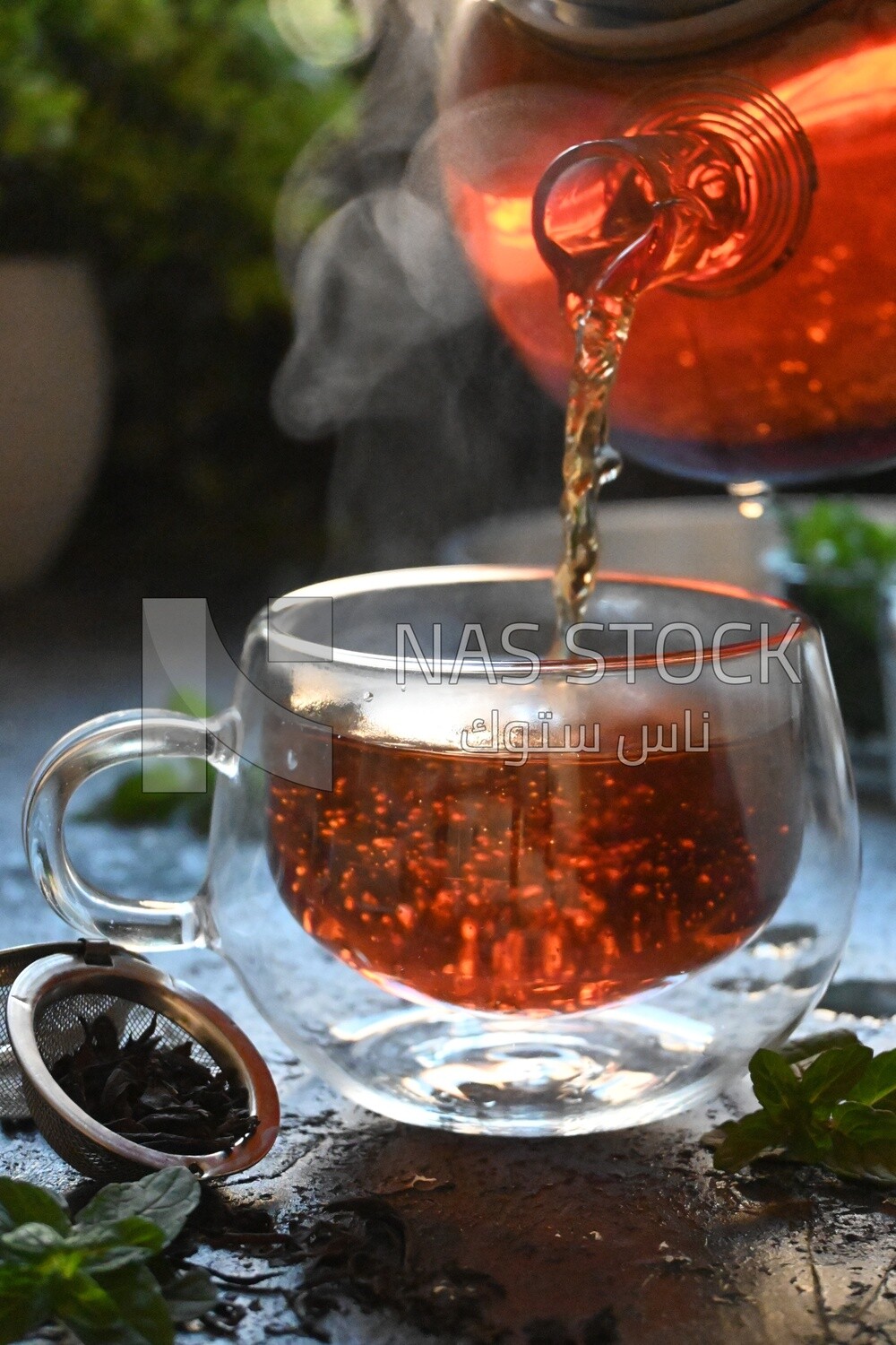 Glass kettle pouring tea from jug to cup of tea