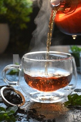 Glass kettle pouring tea from jug to cup of tea